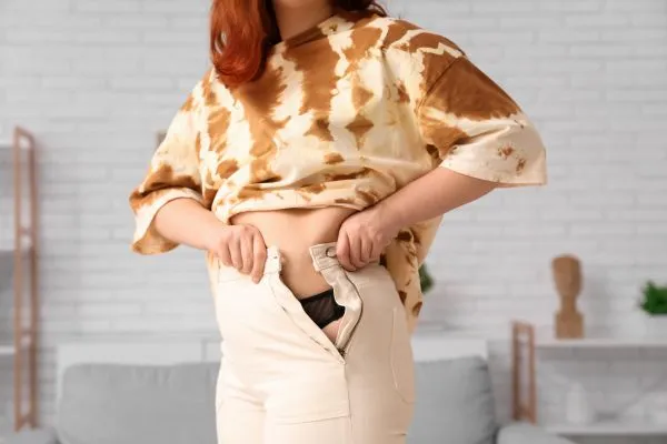 Image of woman trying to do her trousers up after pregnancy weight gain Brighton